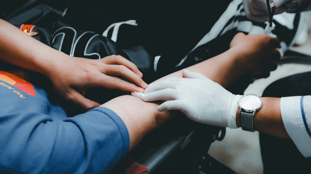 A close-up of a gloved hand holding a patient's arm during a blood donation, offering comfort and care