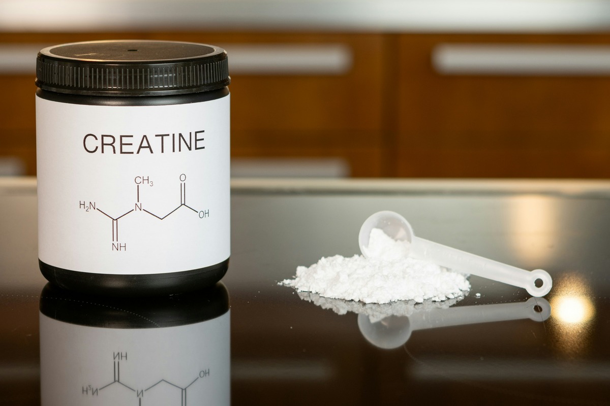 Creatine supplement jar with chemical structure label, next to a scoop of powder on a shiny surface