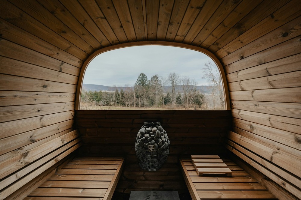 Wooden sauna interior with a heater and a window offering a serene view of trees and distant hills